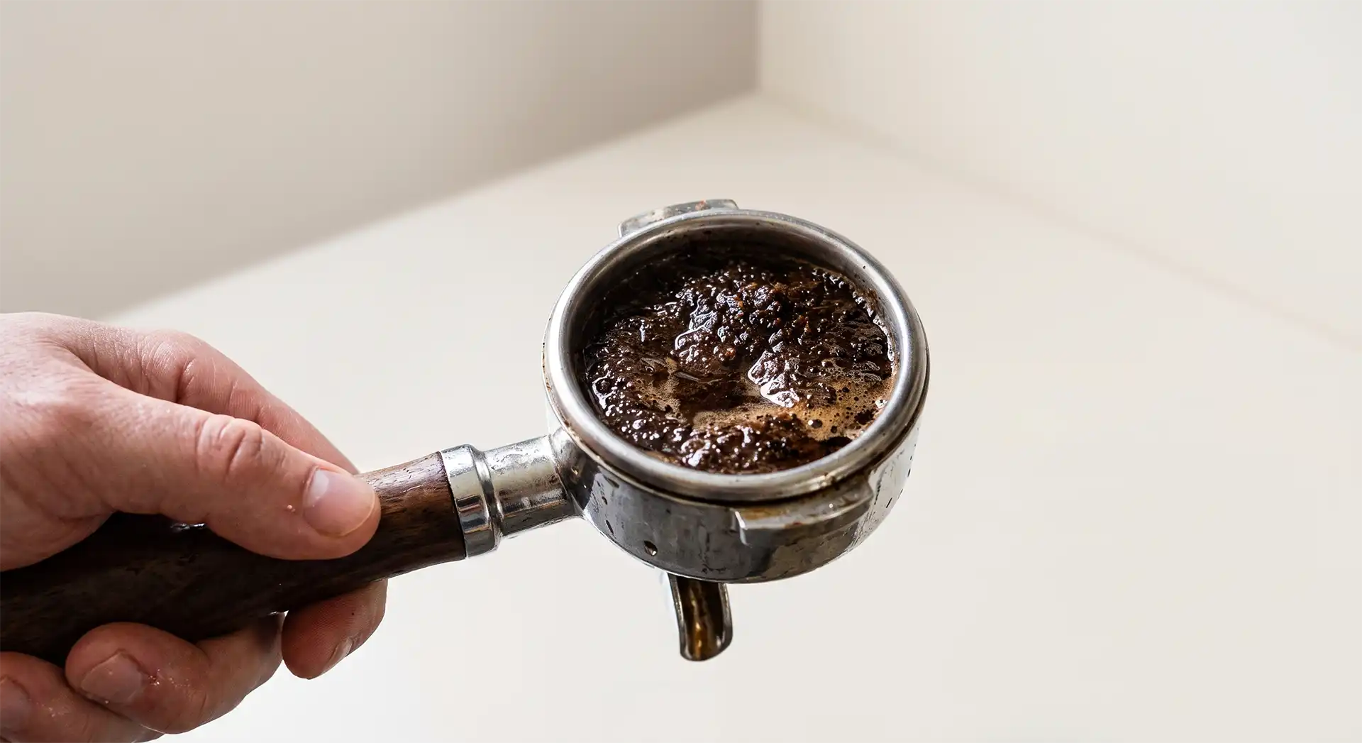 Ein nasser, matschiger Espresso-Puck im Siebträger vor einem minimalistischen, hellen Hintergrund.